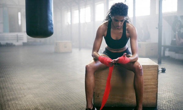 Woman, bandage and boxer wrapping knuckles in gym for self defense, fighting or workout. Fitness, active female person or girl fighter with fist strap on hands for boxing safety, protection or gloves