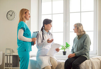 Female doctor and nurse conducting a medical consultation for an elderly patient in a hospital...