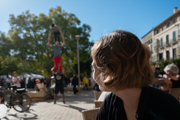 young woman admires circus performance of street acrobats in a street in Malaga, Spain on a sunny...