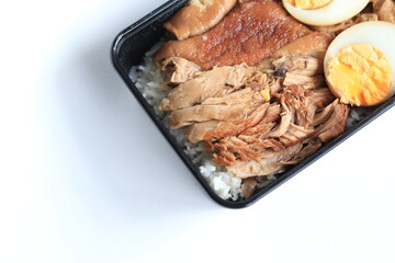Stewed pork leg on rice (kao ka moo) and egg in plastic box on white background. Thai food