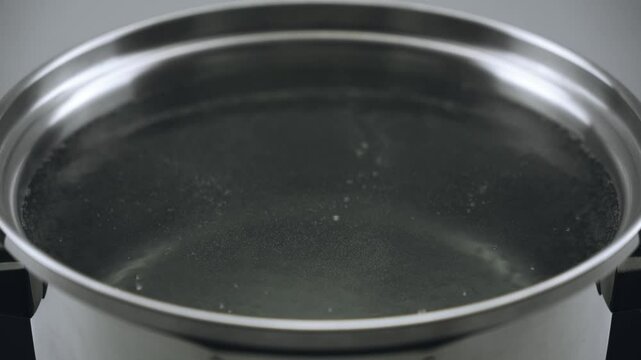 The water starts to boil in the pot. Lots of small bubbles. Close-up. 4k video