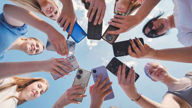 School friends in a circle, sharing content and enjoying time together with smartphones in hand against a sky background