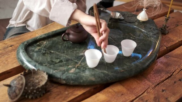 Close-up: a girl in a light shirt prepares for drinking tea, washing the paraphernalia for the tea ceremony with hot water.