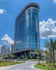 Obraz premium Modern glass building under blue sky with white clouds and palm trees on a sunny day