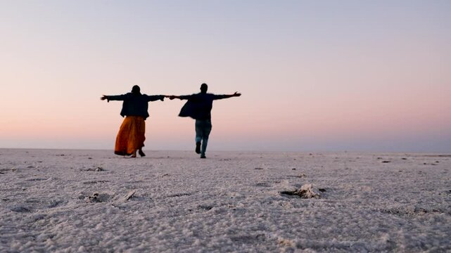 young couple enjoying at remote white salt desert with bright orange sky at morning from low angle video is taken at dhordo kutch white rann gujrat india.