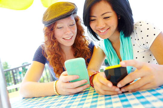 Phone, outdoor and girl friends reading text for planning graduation trip together in group chat. Happy, cellphone and young people at cafe with travel blog for holiday advice, tips or guidance.