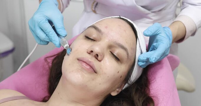 People, beauty, spa, cosmetology and technology concept - Cosmetologist makes the procedure microcurrent therapy of the facial skin of a beautiful, young woman in a beauty salon