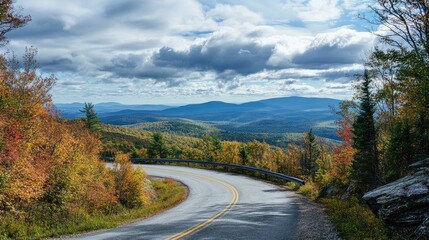 Fototapeta premium Scenic winding mountain road surrounded by vibrant autumn foliage and panoramic landscapes under a cloudy sky
