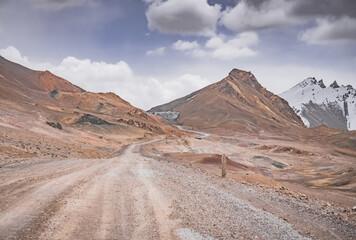 Dusty high-mountain road of Pamir Highway and Ak-Baital Pass, panoramic landscape in rocky mountains with snow in Tien Shan Mountains in Tajikistan