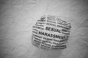 Crumpled paper ball with words Sexual Harassment on torn white paper pieces background.