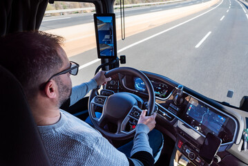Truck driver driving a truck on a highway, with the dashboard, steering wheel, and rearview mirror...
