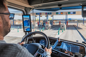 Truck driver operating a heavy vehicle and entering a toll gate marked with "T," a fast lane for trucks, passing through without stopping.