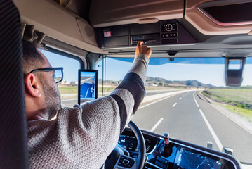 Truck driver driving on a highway while checking the daily work recorded on the tachograph.