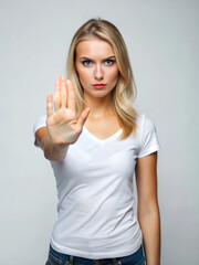 Fototapeta premium A serious young woman in a white shirt raises her hand, signaling to stop, against a neutral background.