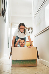 Box, moving house and mother pushing son for having fun or playing game in new home together....