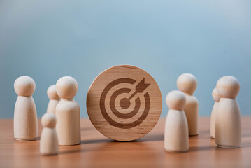 Teamwork and Business Goals Execution. A wooden disc with a bullseye and arrow icon is placed among wooden figures, symbolizing goal setting, business strategy, leadership, and teamwork.