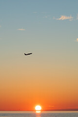 Plane flies at sunset over the sea, evening silhouette and orange sky, aviation journey and freedom in the clouds.