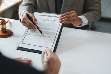 Lawyer pointing with a pen to the signature line on a contract, while a gavel sits blurred in the...