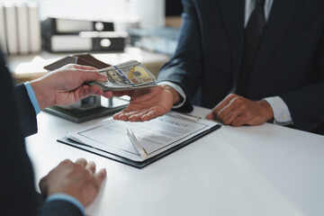Two businessmen in suits exchanging money over a signed contract with a miniature house and pen on...