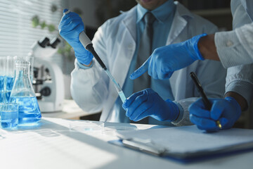 Professional chemists wearing lab coats and gloves are conducting experiment using pipette and test...