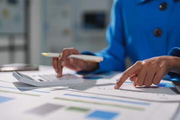 Businesswoman examining financial reports, using calculator and pointing at charts, performing...