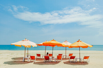 Woman sit on the orange umbrella chair set on the beach with blue sky.