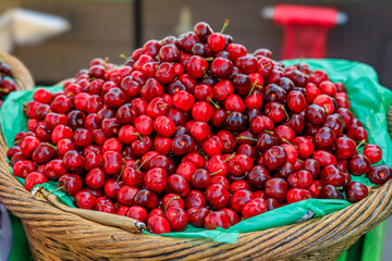 Heaps of fresh red cherries displayed in a wicker basket on a stand at a farmers market in San Francisco, California