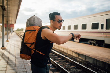 Man tourist backpacker look at the watch wait for the train.