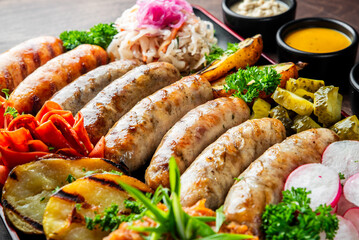 A colorful platter featuring an assortment of grilled sausages accompanied by fresh vegetables, pickles, and sauces, all arranged on a rustic wooden background. Perfect for food lovers.