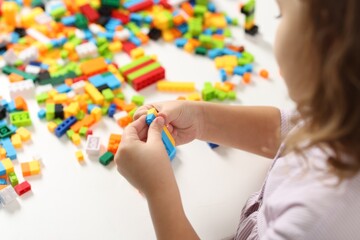 Girl playing with building blocks at white table indoors, closeup