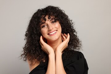 Beautiful young woman with long curly hair on light grey background