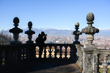 A tourist take a photo of Turin city (Torino) from Villa della Regina viewpoint. Mole Antonelliana and snowy Alps mountains on background. Piedmont, Italy