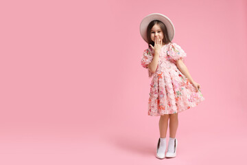 Stylish little girl wearing oversized high heeled shoes on pink background, space for text