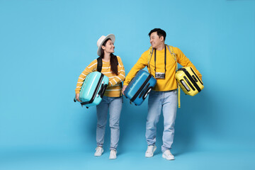 Happy travellers carrying suitcases on light blue background