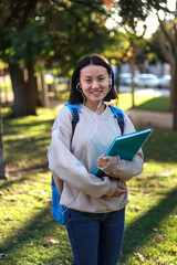 Fototapeta premium Smiling Asian student carrying a notebook and backpack outdoors