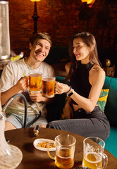 boy and girl clink glasses of beer cheerful mood evening light