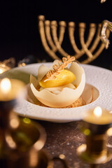 A dessert with a yellow center and a white shell is on a white plate. The dessert is surrounded by candles, which give the image a warm and cozy atmosphere
