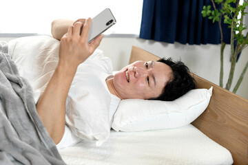 ベッドの上でスマホを持ちながら困る男性