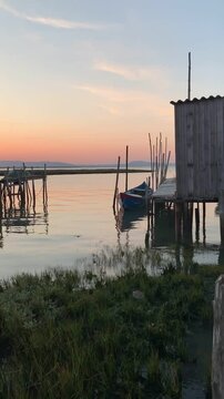 Wooden pier with a small boat on calm water at sunset in Comporta, Portugal