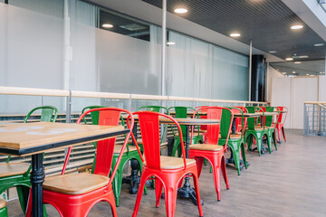 Modern indoor seating area with colorful red and green metal chairs and wooden tables on a hardwood floor, set in a bright open space.