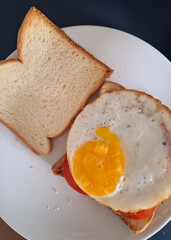 Egg sandwich: sunny side up, tomato, and lettuce on white breads served on white plate
