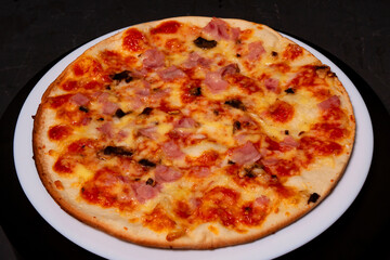 Pizza with ham and mushrooms on a white plate. Black background.