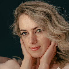 A close-up portrait of a stylish woman with wavy blonde hair, elegant silver rings, and soft...