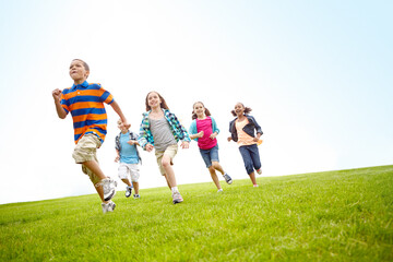 Playing, running and group of kids on grass for outdoor games, race and happy development. Diversity, energy and children in field together with smile, growth and fun summer weekend on low angle.