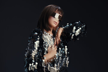 Woman in sequinned dress with sunglasses on head, hands on hips, confidently posing against a black...