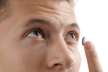 Man putting color contact lens in his eye on white background, closeup