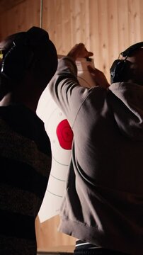 Vertical video Man holds rifle, enjoying recreational shooting experience in firing range next to group of friends. People practicing with weapons in safe environment at shooting range company, camera