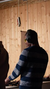 Vertical video Group of friends in firing range doing recreational shooting activity with firearm, hitting bullseyes. People in shooting gallery training with handguns, sharpening skills, camera A