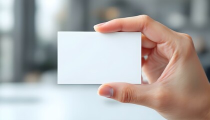 Obraz premium A hand holding a blank white card, close-up focus, with a blurred professional background, creating a clean and minimalistic look.