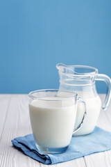 milk in glass cup and in jug on table on the blue background